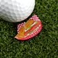 A close-up of a golf ball on artificial grass beside Ballmarkers by Logie Joes Breaded Tenderloin Basket—a premium, humorous ball marker featuring a fried chicken sandwich and fries on a red checkered tray.