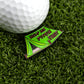 A white golf ball sits on artificial grass beside Ballmarkers by Logie Joes Pitch That Tent enamel pin—a funny, premium ball marker shaped like a green tent and perfect for golfers seeking unique accessories.