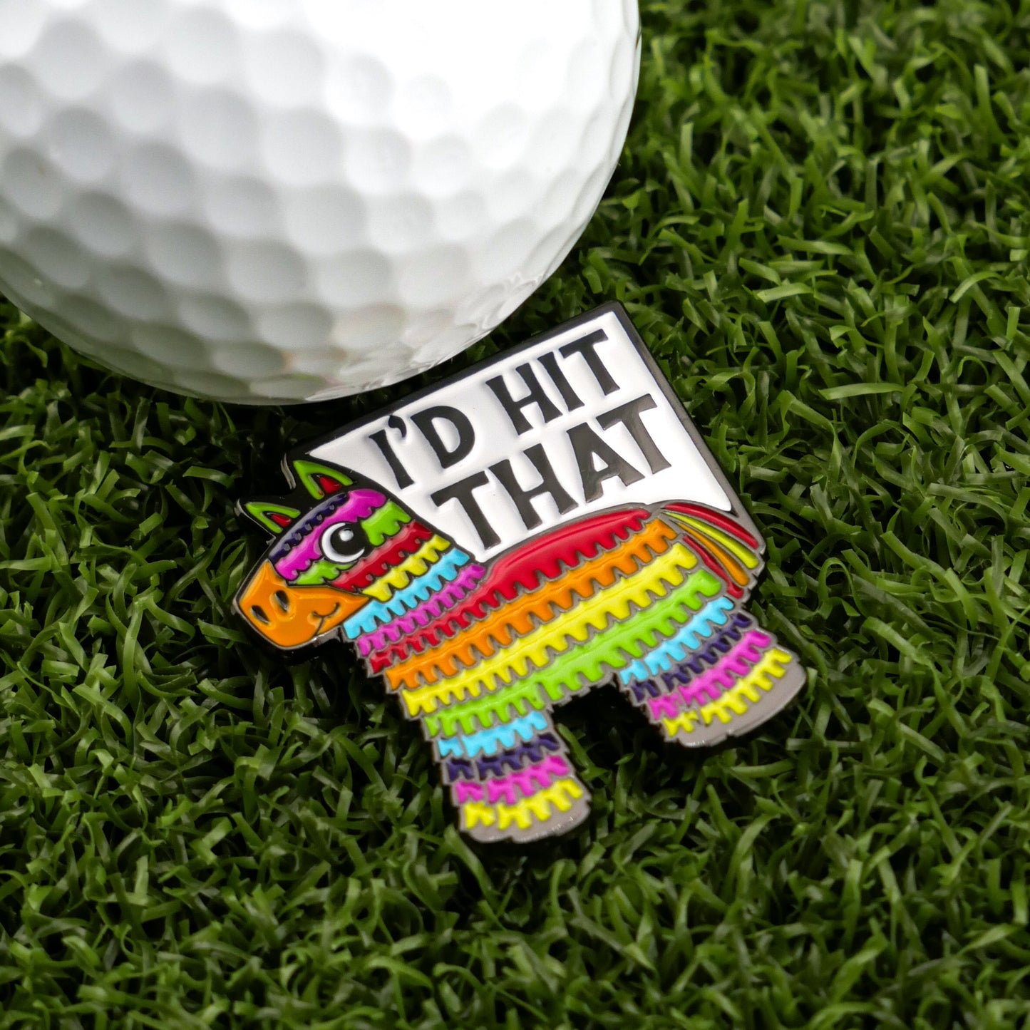 The I’d Hit That Piñata by Ballmarkers from Logie Joes is a rainbow-striped donkey pin with “ID HIT THAT,” shown on grass beside a golf ball—a fun, unique marker for fans of humorous golf accessories.